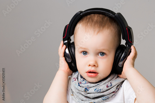 Fun and cute smiling little boy listening music in earphones and having fun. Stylish wearing in white t shirt and scarf, with blue eyes and pure skin, having fun.