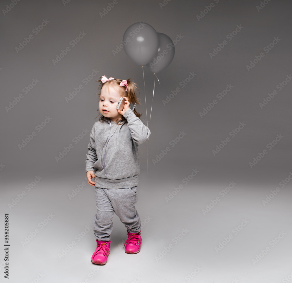 Φωτογραφία Portrait of stylish little girl in gray suite posing at studio, walking and talking to call phone