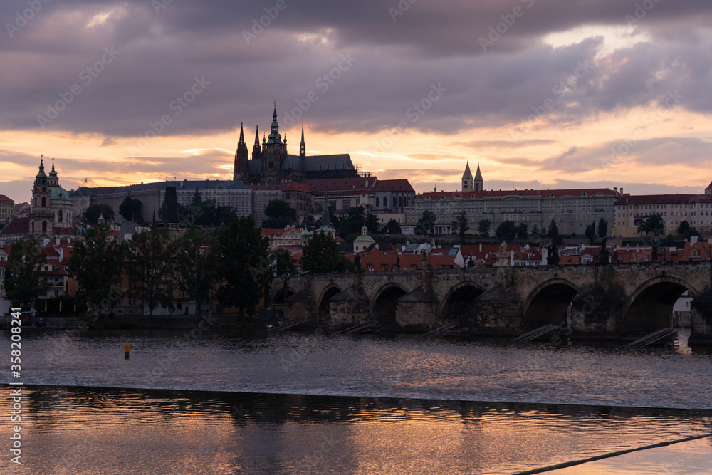 Obraz premium Charles Bridge, Prague Castle, St. Vitus Cathedral and the flowing Vltava River and the roofs of buildings at sunset in the center of Prague in the Czech Republic in summer