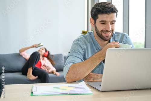 Morning coffee time lifestyle of young couple lover wearing casual dress together working on laptop notebook computer in living room at home.