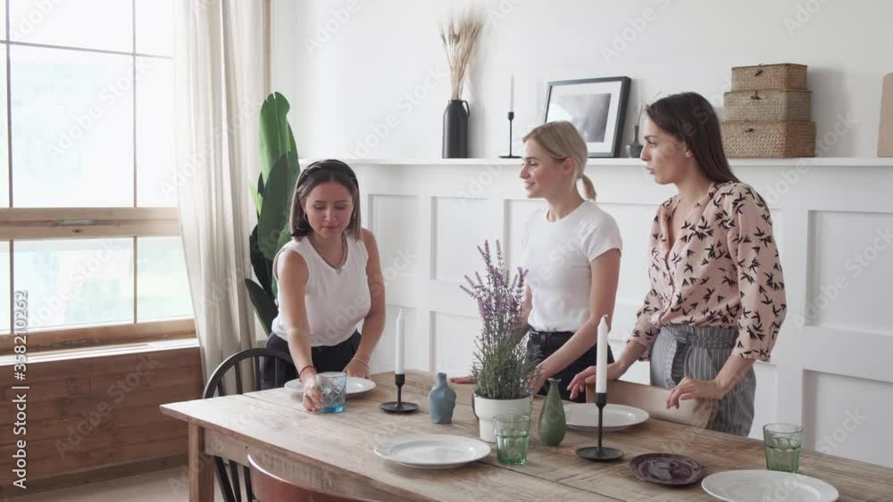 Three girls are smiling standing in the kitchen and laying out plates for a joint dinner Three girls are smiling standing in the kitchen and laying out plates for a joint dinner