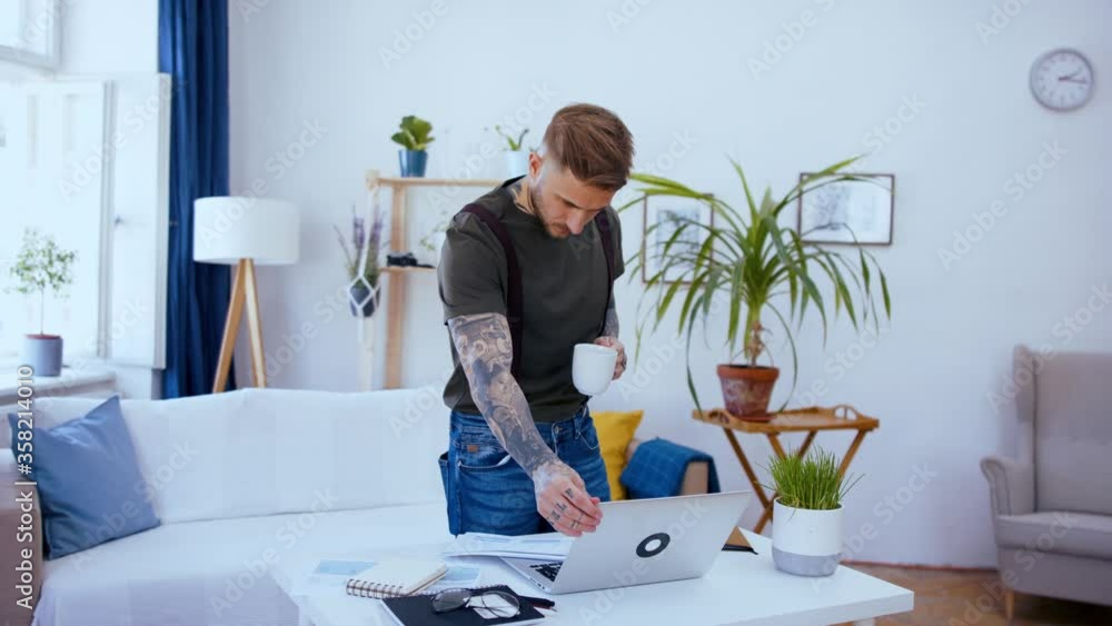 Man with laptop standing indoors at desk in home office, working. Man with laptop standing indoors at desk in home office, working.