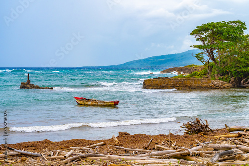 Seascape coastline setting on tropical Caribbean island. Old wooden fishing boat floating in shallow water near white sand seashore on coastal beach with debris/ driftwood/ drift wood/ bamboo logs. photo