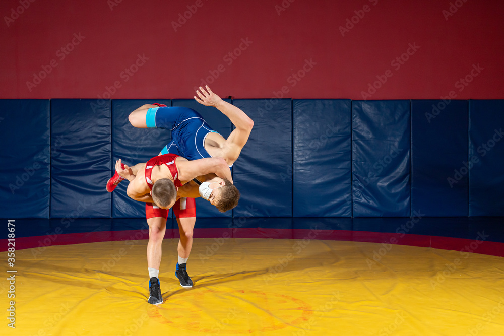 The concept of fair wrestling. Two greco-roman  wrestlers in red and blue uniform wrestling   on a yellow wrestling carpet in the gym