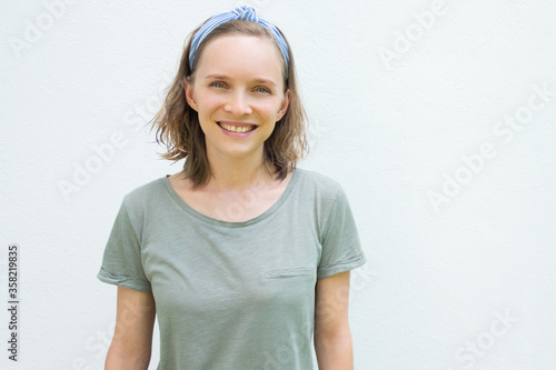 Happy cheerful woman in hairband and t-shirt looking at camera, smiling. Person posing isolated against white wall. Front view. Summer tourist outfit concept photo