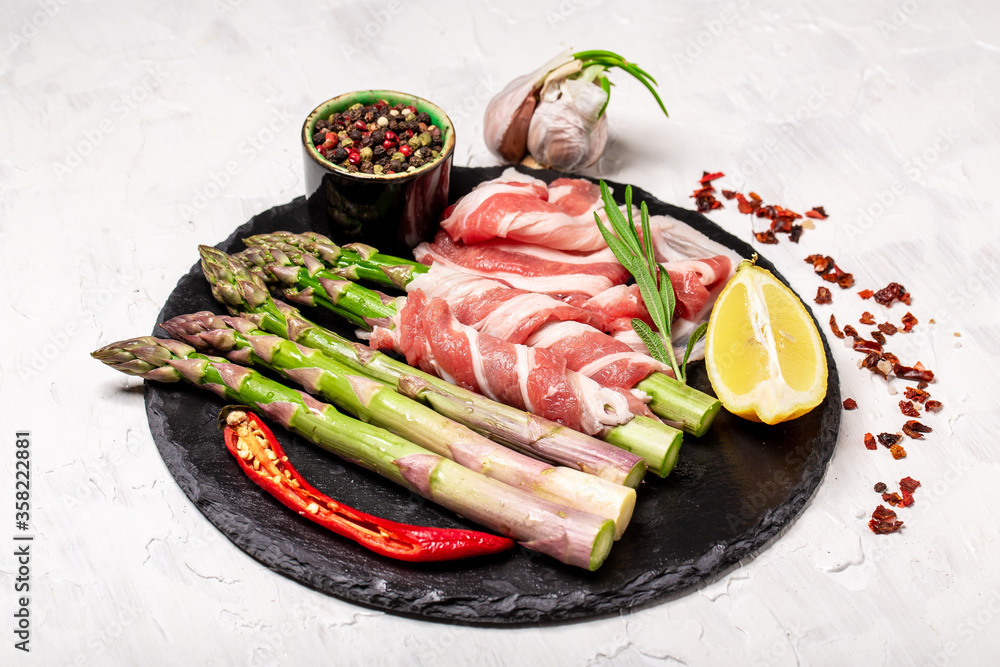 Close Up of Asparagus Wrapped in Bacon with Curl of Butter on Rustic Wooded Board Surrounded by Raw Ingredients