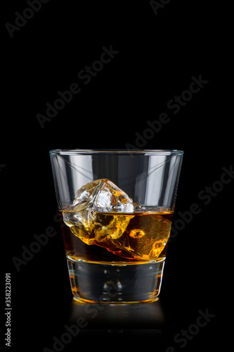 Glass of whiskey with cube ice on black background