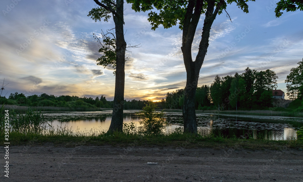 image with a beautiful colorful sunset over the lake, in the foreground the contours of trees and grass, Lielais Ansis, Rubene, Latvia image with a beautiful colorful sunset over the lake, in the foreground the contours of trees and grass, Lielais Ansis, Rubene, Latvia