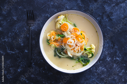 healthy plant-based food recipes concept, vegan soup with fresh veggies topping incuding caulini carrots onions and broccolini photo