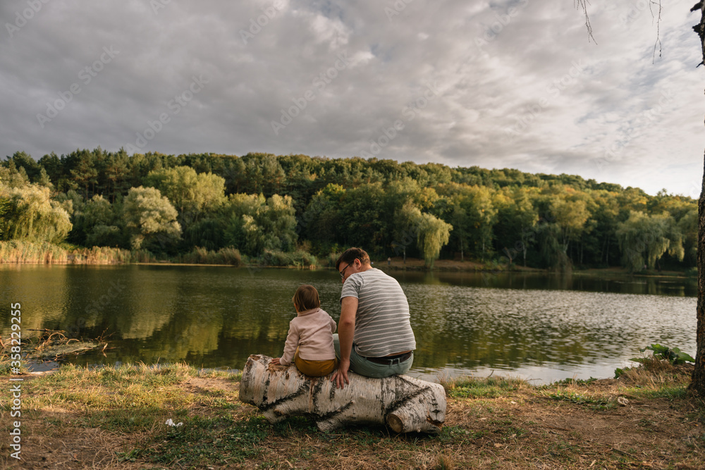 Father and baby girl sitting near lake. Local travel. New normal vacation. Father's day Father and baby girl sitting near lake. Local travel. New normal vacation. Father's day