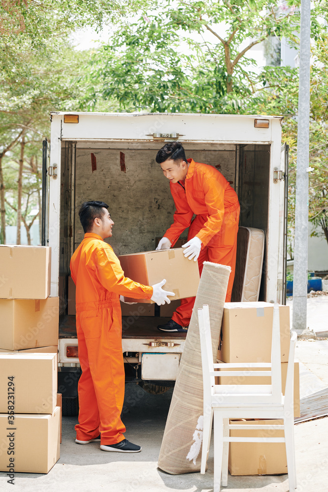 Two young adult men working in modern house moving service loading lorry with boxes, vertical shot