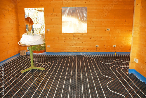 A hydronic closed loop underfloor heating system laid out on a molded insulated panel in EPS with a spooling table inside a partially constructed wooden house

