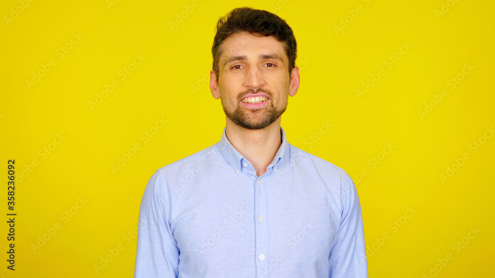 Fototapeta premium Handsome bearded man in a light blue shirt smiles. Businessman looking at the camera on a yellow background with place for text