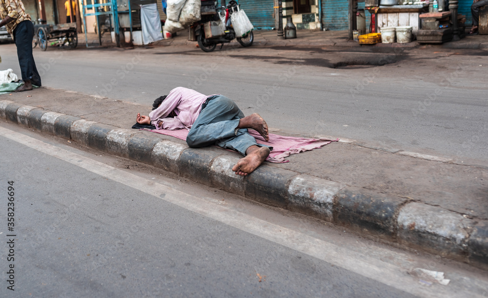 A homeless man sleeping on the street footpath during the day time. A ...