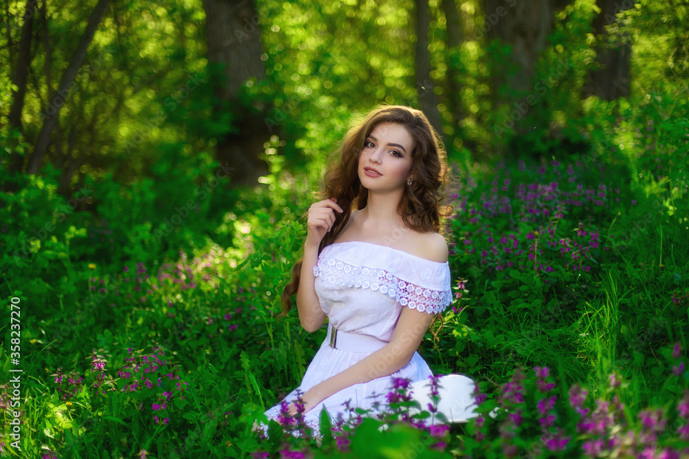 Closeup portrait of attractive young girl with long curly hair sitting on grass. She wears white dress Closeup portrait of attractive young girl with long curly hair sitting on grass. She wears white dress