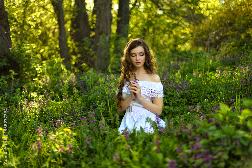 Beautiful young girl in white dress sits on the grass in spring garden Beautiful young girl in white dress sits on the grass in spring garden