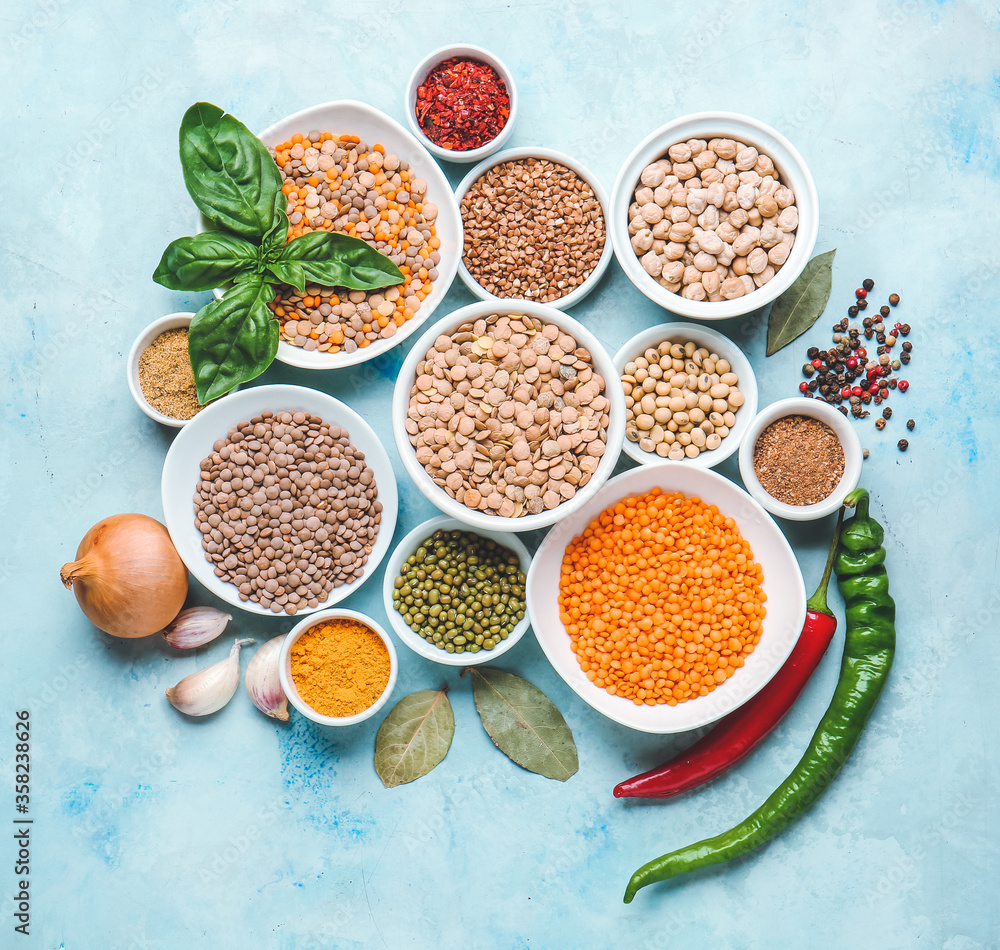 Bowls with lentils and spices on color background