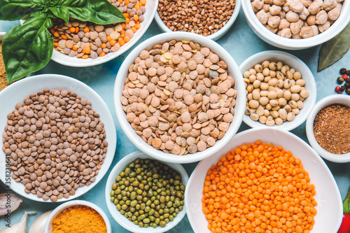 Bowls with lentils and spices on color background