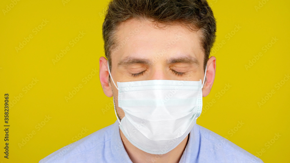 Closeup man with eyes closed in a protective medical mask. Head on a yellow background. Concept against the virus: Coronavirus, flu