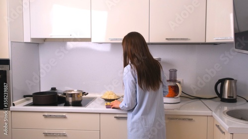 Young and beautiful housewife woman cooking in a white kitchen.