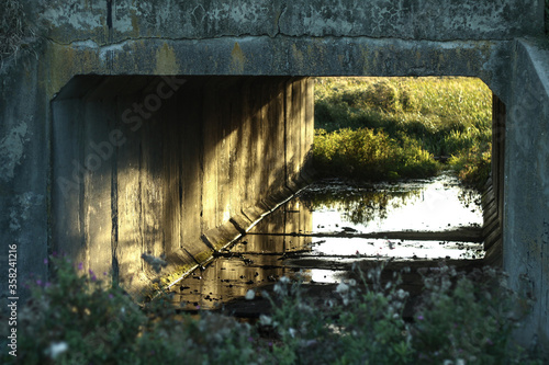 Small tunnel along the road filled with water at sunset day. Concrete landscape