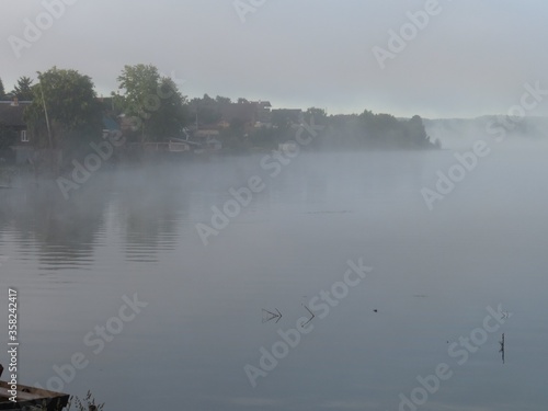 Wet grass on a lake coast in foggy morning