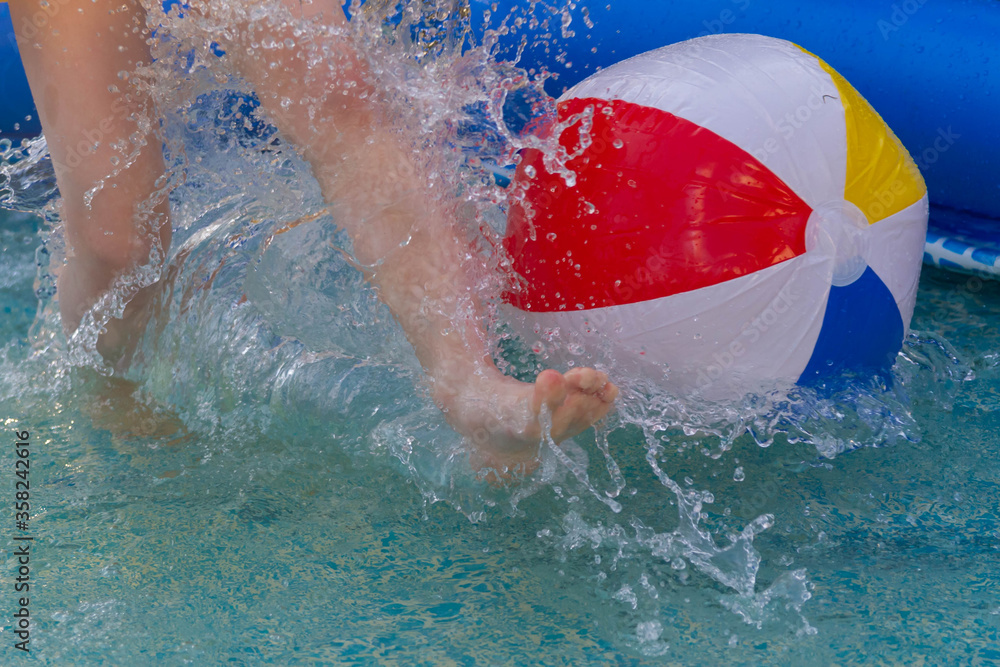 A child kicks an inflatable ball in the water. A spray of water.