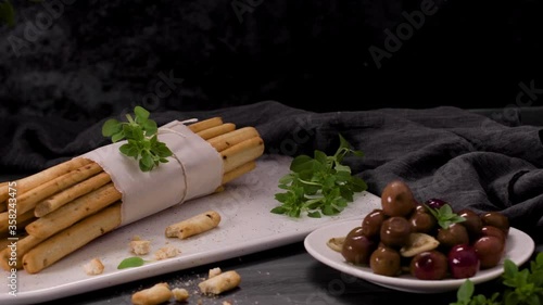 Fresh baked homemade grissini bread sticks in white ceramic tray with olive oil and basil herbs over kitchen counter top. photo