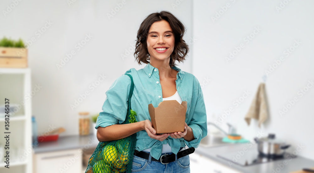 sustainability, food shopping and eco friendly concept - happy woman in turquoise shirt and jeans holding reusable net bag with fruits and vegetables and takeaway wok box over home kitchen background sustainability, food shopping and eco friendly concept - happy woman in turquoise shirt and jeans holding reusable net bag with fruits and vegetables and takeaway wok box over home kitchen background