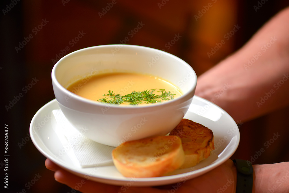 A waiter wearing plaid uniform serving a bowl of hot soup in a restaurant. Concept for a tasty and healthy meal. A waiter wearing plaid uniform serving a bowl of hot soup in a restaurant. Concept for a tasty and healthy meal.