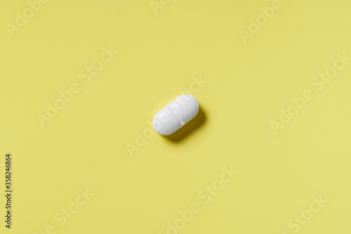 White pill on a yellow background. Hard light. Paper background