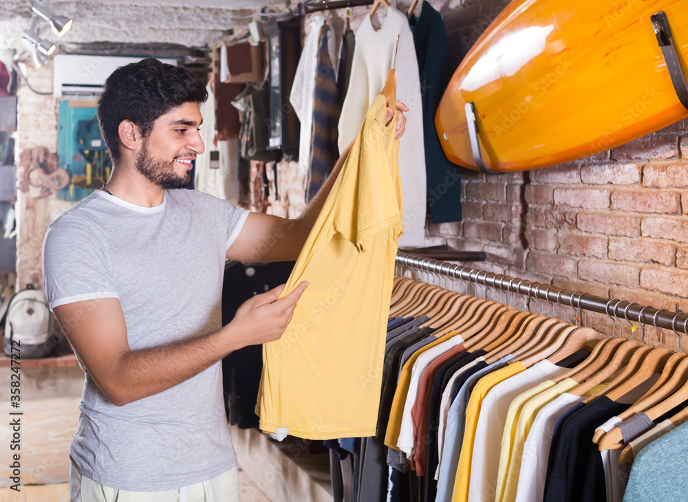 smiling male buyer choosing t-shirt in the dress shop