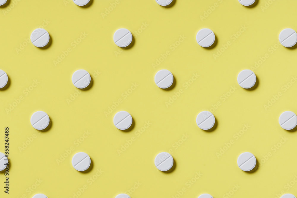 Pattern of white rouned shaped pills on a yellow background. Hard light. Paper background Pattern of white rouned shaped pills on a yellow background. Hard light. Paper background