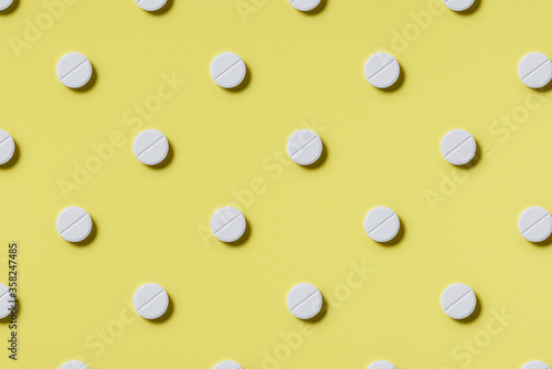 Pattern of white rouned shaped pills on a yellow background. Hard light. Paper background