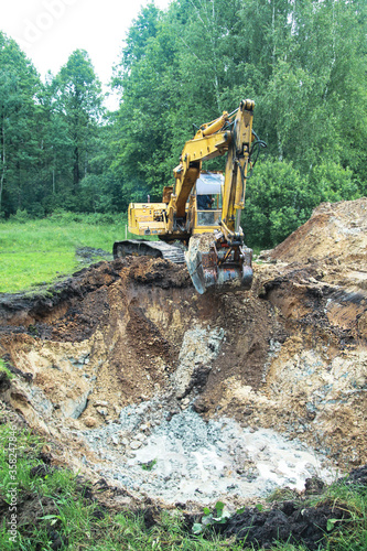 An excavator digs a large trench for building a house. A tractor digs a large lake that is already gaining water. Stock background for design © subjob