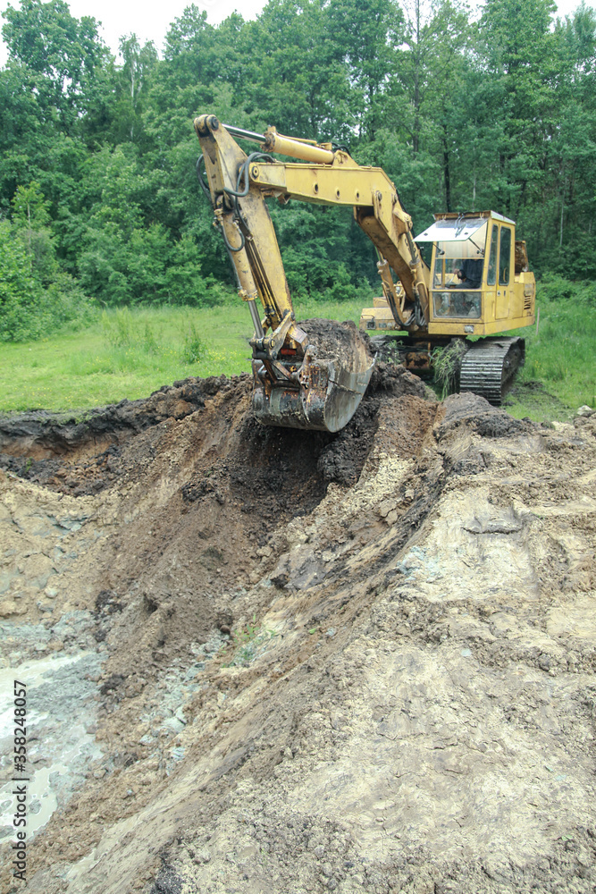 Obraz premium An excavator digs a large trench for building a house. A tractor digs a large lake that is already gaining water. Stock background for design