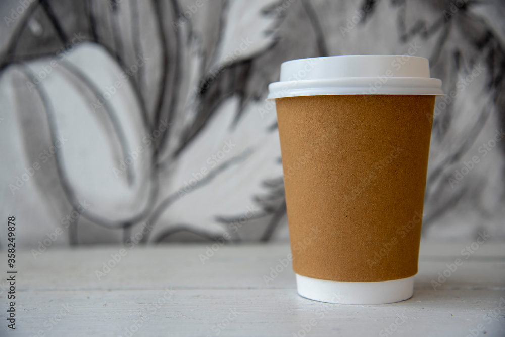 A cardboard Cup of coffee against a patterned wall . A cardboard Cup of coffee against a patterned wall .
