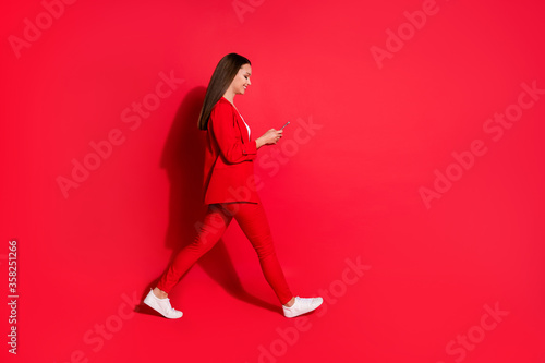 Full size profile photo of beautiful business successful lady walk conference seminar meeting browsing telephone busy wear blazer pants suit white footwear isolated red color background