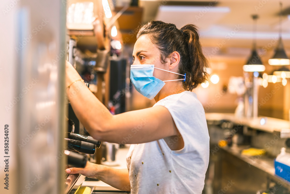 Photo session with a waitress with a face mask in a bar. New normality, security measures after the coronavirus pandemic, social distance, covid-19. Preparing coffees in the machine