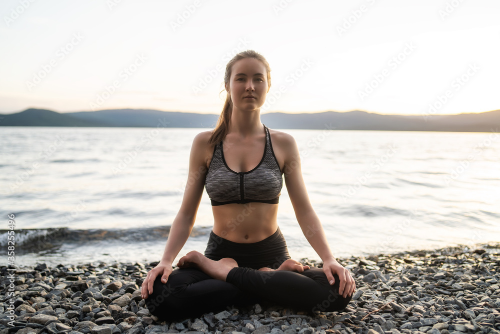 Beautiful girl in a yoga pose on the lake. Lotus position