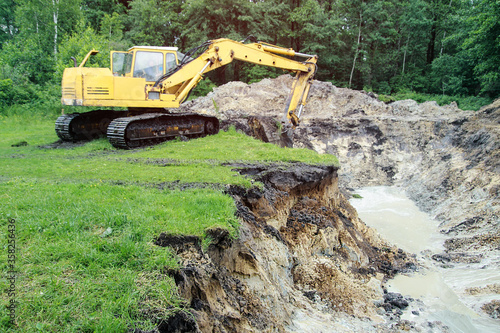 An excavator digs a large trench for building a house. A tractor digs a large lake that is already gaining water. Stock background for design