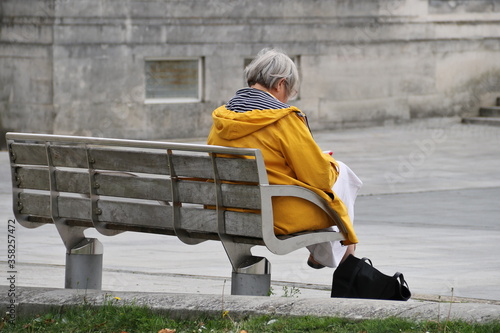 eine ältere Frau  - Rentnerin sitzt allein und einsam auf einer Bank
