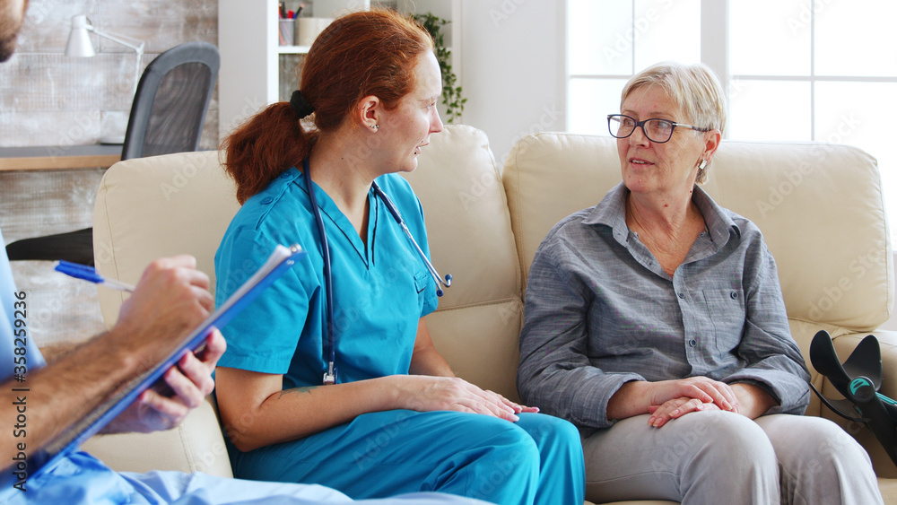 Obraz premium Male assistant writing rehabilitation treatment for senior woman while female doctor is talking with her