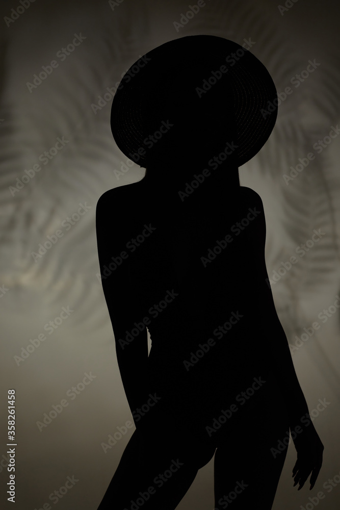 silhouette of slim woman in swimsuit and hat posing on studio background. silhouette of slim woman in swimsuit and hat posing on studio background.
