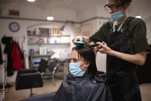 Hairdresser and girl child customer in a salon with medical masks during virus pandemic. Working with safety mask.