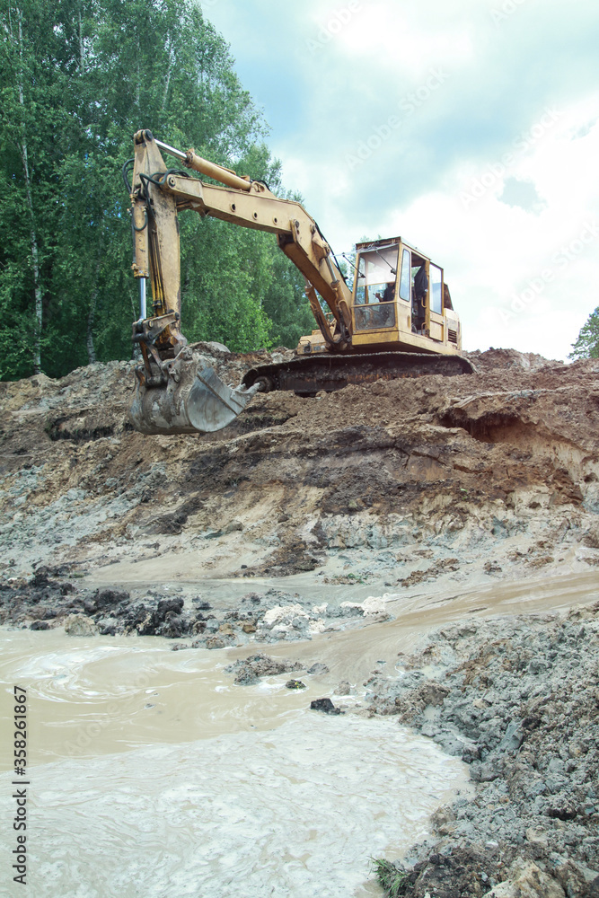 Fototapeta premium An excavator digs a large trench for building a house. A tractor digs a large lake that is already gaining water. Stock background for design