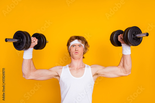 Close-up portrait of his he nice attractive sportive funky muscular nerd guy sportsman lifting heavy barbell physical intense isolated over bright vivid shine vibrant yellow color background