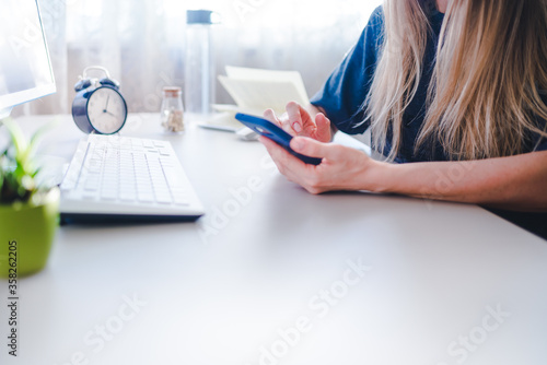 young woman sits at a desk and types on a smartphone