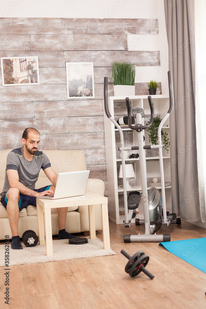 Fototapeta premium Man in sportswear searching body exercise on laptop during global pandemic.