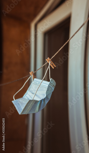 A white medical protective mask hanging is dried on the balcony next to the washed laundry.